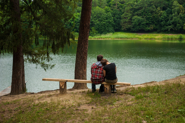 Ein junges Paar sitzt auf einer Bank und blickt auf einen See.