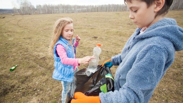 Ein Mädchen und ein Junge sammeln Müll in einem schwarzen Müllsack.