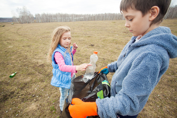 Ein Mädchen und ein Junge sammeln Müll in einem schwarzen Müllsack.