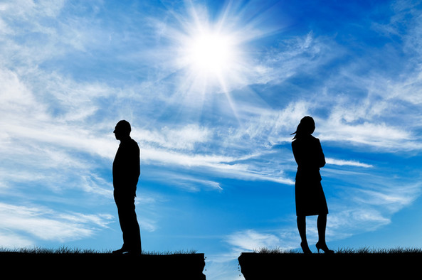 Silhouette eines Mannes und einer Frau, getrennt durch einen Spalt in der Erde vor blauem Himmel