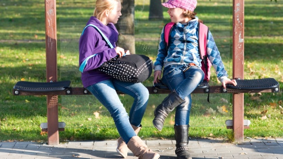 Zwei Mädchen an einer Bushaltestelle unterhalten sich.
