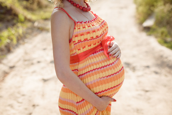 Frau in einem orange-gemusterten Kleid umfasst ihren schwangeren Bauch.