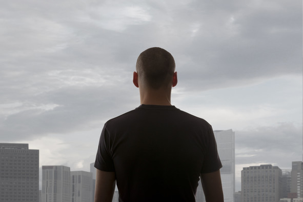 Ein junger Mann steht an einem Fenster mit Blick auf Hochhäuser.