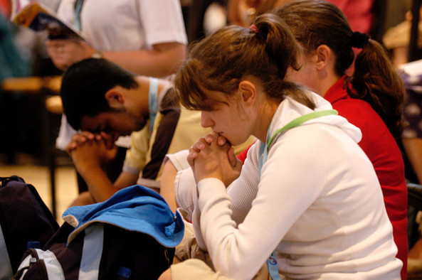 Zwei junge Menschen beten im Sitzen mit gefalteten Händen beim Weltjugendtag.