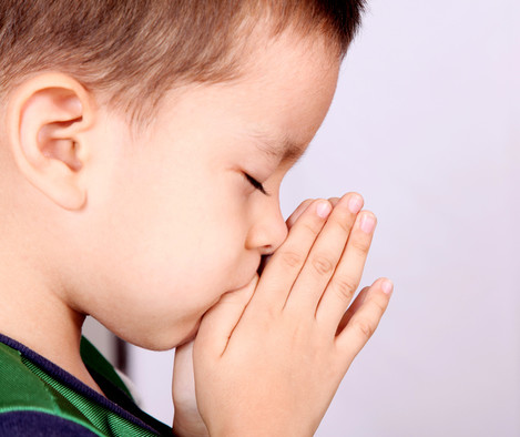 Ein Junge betet mit geschlossenen Augen und gefalteten Händen.
