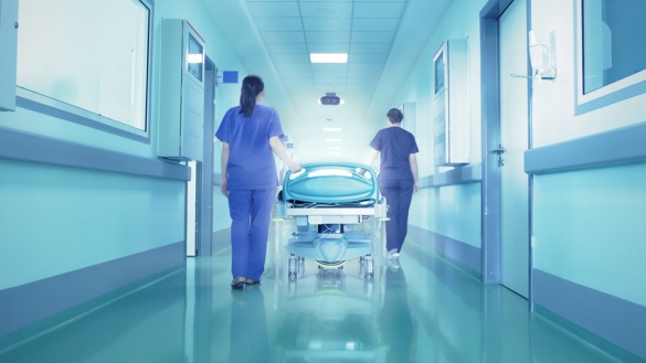Zwei Krankenschwestern schieben ein leeres Bett über den Krankenhausflur.