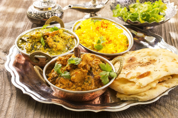 Ein Tablett mit zwei verschiedenen Currygerichten, gelbem Reis und dem indischen Brot Naan.