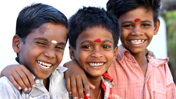 Drei lachende Jungen mit einem weißem oder einem roten Punkt auf der Stirn.