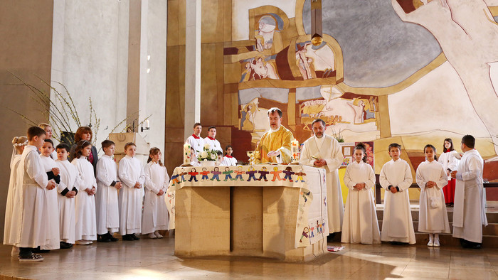 Kinder in weißen Gewändern stehen im Halbkreis hinter dem Altar und Pfarrer