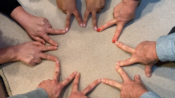 Neun Hände formen mit ihren Zeige- und Mittelfingern einen neunzackigen Stern auf dem Boden