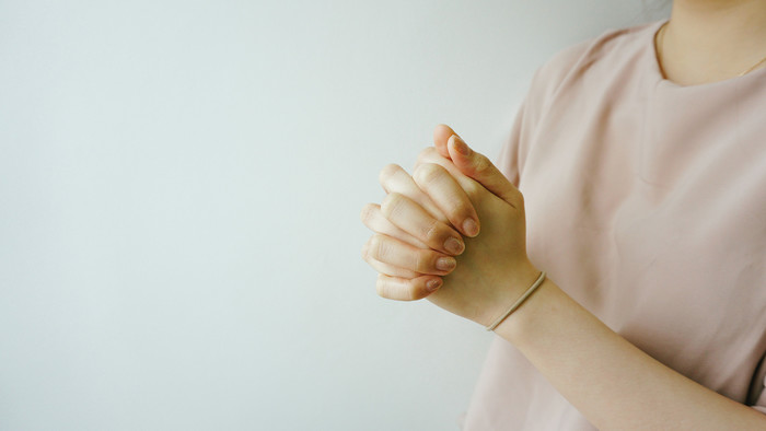 Frau in rosa Oberteil hat die Hände gefaltet und die Finger in einander verschränkt.