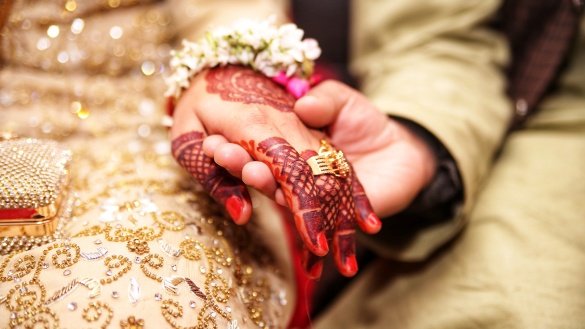 Frauenhand, verziert mit Henna-Mustern und einen goldenen Ring am Finger, wird gehalten von einer Männerhand.